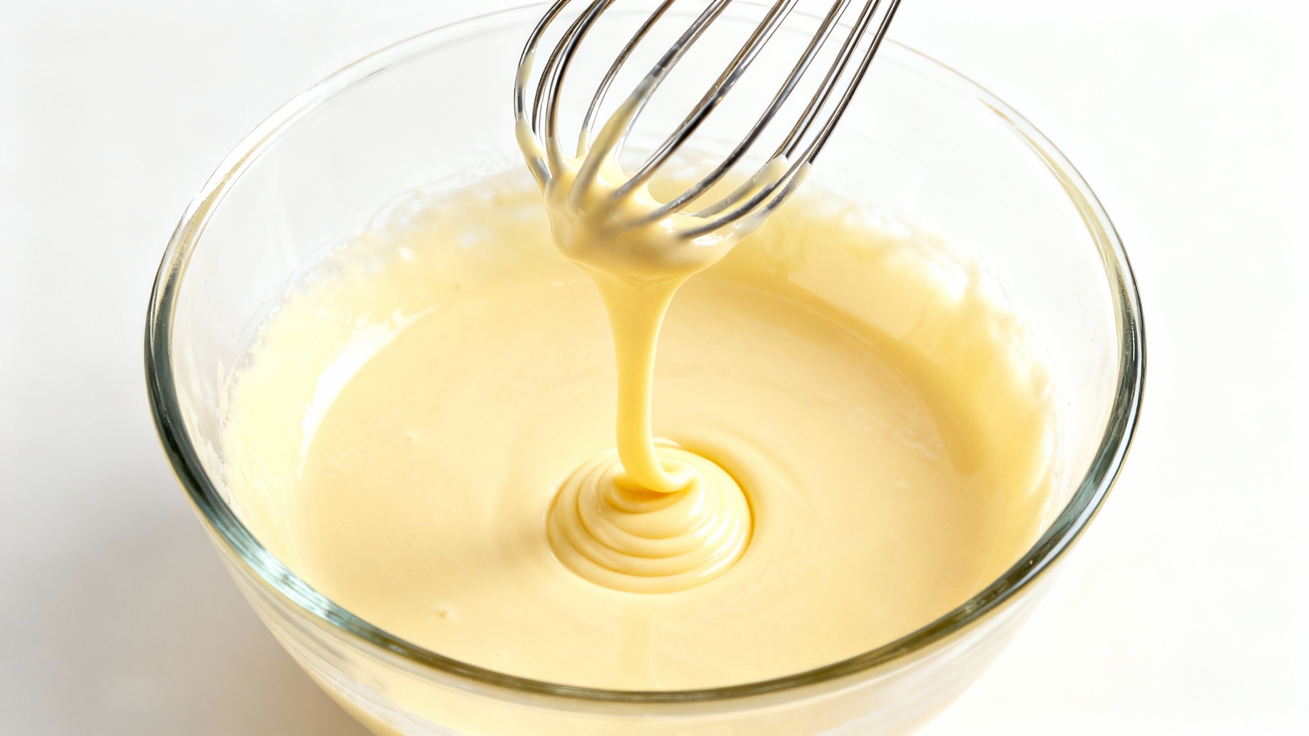 Close-up de ovos e açúcar batidos até o ponto de fita em tigela de vidro, o segredo para criar a casquinha crocante do brownie perfeito